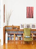 Large CD collection and books on pale wooden shelving behind comfortable vintage reading chair on castors