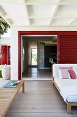 Summery wooden veranda with comfortable, upholstered lounger and bench in front of open, slatted door
