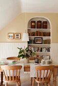 Wooden dining table with lath back dining chairs in room an alcove bookshelf