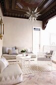 White, delicate wooden chair and floor cushions around small, white coffee table in elegant, Oriental loggia with dark, ornate wooden ceiling