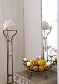 Wire candlestick used as fruit basket on wicker table and large mirror in corner of bright room