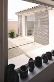 Heads and containers made of black material on a window ledge and a view of a courtyard with sliding architectural elements on the home's facade