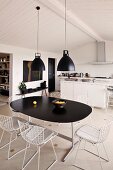 Retro hanging lamps above a dining table with black top and chairs with white metal frames in a functional kitchen