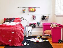 Girl's bedroom with red bed linen with heart motif; pink bins and wire baskets on wall for storing toys