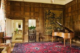 Grand piano with natural wood finish in room with coffered wooden walls and view into hallway through open door