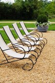 Elegant deckchairs with black metal frames and canvas seats on gravel in garden