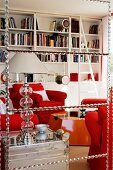 Blick durch Raumteiler ohne Füllung aus Metall auf rote Polstersesseln vor modernem, weißem Einbauregal