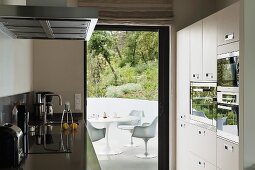 Designer kitchen with appliances in fitted cupboards and view of white, plastic Bauhaus chairs through open terrace door