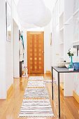 Narrow hallway with white, paper pendant lamps above rugs on wooden floor and wooden front door at far end
