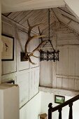 Stairwell with wrought iron pendant lamp hanging from exposed, wood-clad roof structure and antlers on wooden wall