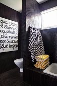 Modern bathroom with black mosaic tiles and striped towels hanging on toilet screen wall