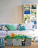 DIY coffee table made from green glass sheet on stacked magazines in front of sofa and white shelving against wall