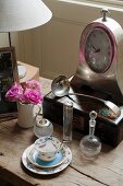Demitasse with saucer and antique glass bottles in front of old mantel clock on wooden table