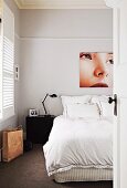 Large-format photo showing detail of woman's portrait above double bed with black bedside table and retro lamp