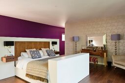 Freistehendes Doppelbett an halbhoher Rückwand mit modernen Nachttischleuchten und elegante Stehlampen beidseits eines Schminktisches