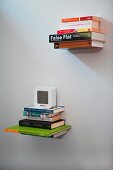 Bücherstapel an weißer Wand hängend, Aufhängung ist unsichtbar