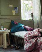 Glass of water on bedside table next to single campstyle bed with cat on window sill above