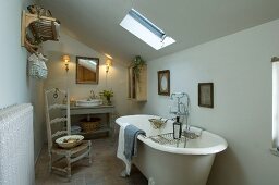 Einfaches Badezimmer unter dem Dach mit freistehender, antiker Badewanne und einem Binsenstuhl mit hoher Rückenlehne; am Boden Terrakottafliesen