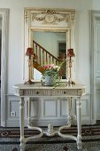 Grey console table below mirror with ornate frame reflecting staircase