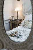 Corner of room with nostalgic bed, lit bedside lamp and breakfast tray reflected in mirror