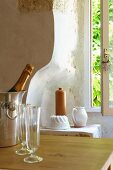 Bottle of sparkling wine and wineglasses on wooden table in front of earthenware pots in niche