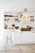 White, open-plan kitchen with magnificent chandelier above island counter