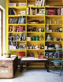 Coffee table next to vintage leather trunk in front of yellow-painted shelving holding crockery and books