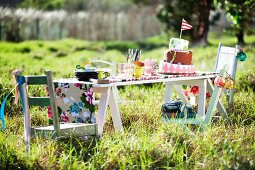 Mehrstöckige Torte mit Fähnchen und Geschirr für Kindergeburtstag auf einfachem Holztisch in der Wiese