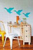 Aufklappbarer, platzsparender Tisch aus Holz mit kleinen Schubladen; an der Wand drei fliegende Enten