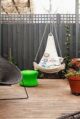 Suspended wicker chair next to planter and other seating on terrace in front of grey screen