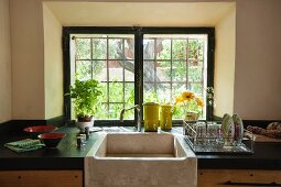 Kitchen counter with black worksurface and large stone sink below window with original glazing