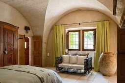 Rustic bedroom with historical stone vaulting; designer sofa with wire frame next to enormous urn