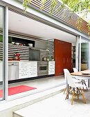 View into contemporary fitted kitchen through open sliding glass walls leading to terrace