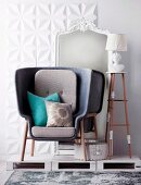 Modern, gray armchair standing in front of white, baroque mirror on white wooden pallets
