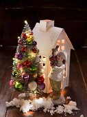Paper house, porcelain figurine and artificial fir tree