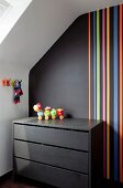 Black chest of drawers against black wall with multicoloured stripes in attic room
