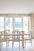Muted dining room in clear natural shades with floor-to-ceiling windows, solid, pale wooden table and white vintage chairs