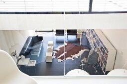 Minimalistischer Wohnraum in Schwarz und Weiß mit langem Wandregal und Kuhfellteppich durch die Glaswand der Galerie betrachtet