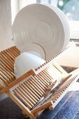 White crockery and silver knives in pale wood draining rack
