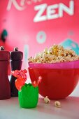 Freshly-made popcorn in pink bowl next to salt and pepper grinders