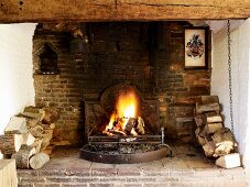 Open fire flanked by stacked firewood in inglenook fireplace