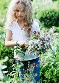 Blonde girl picking flowering herbs in garden