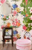 Mirror on wall with floral wallpaper above side table and pouffe