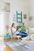 Junge Frau sitzt in einem gemütlichen Wohnzimmer mit Vintage-Möbeln, gestricktem Teppich und gestreifter Tapete