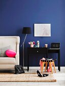 Black console table next to partially visible couch with white leather upholstery against royal blue wall