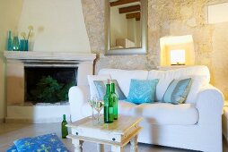 Sofa with white upholstery next to fireplace in Mediterranean living room with stone walls
