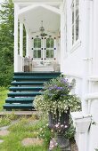 Entrance area with nostalgic, white veranda and wooden steps painted petrol blue behind planted urn