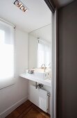 Mirrored wall with enlarging effect behind modern washstand in small bathroom niche