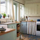 Wohnküche im Landhausstil mit Fronten in Creme und Pastellblau, Retrokühlschrank und Blümchenvorhang