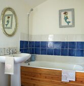 Wood-clad bathtub in small bathroom with picture of mermaid above blue and white tiles